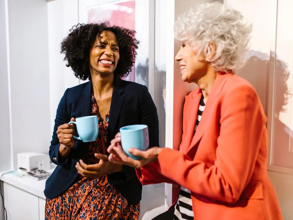 Two people talking over coffee mugs in a bright room, mid-conversation