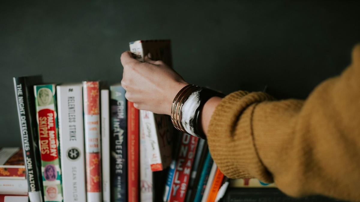 A hand pulling a book from a row of books on a shelf